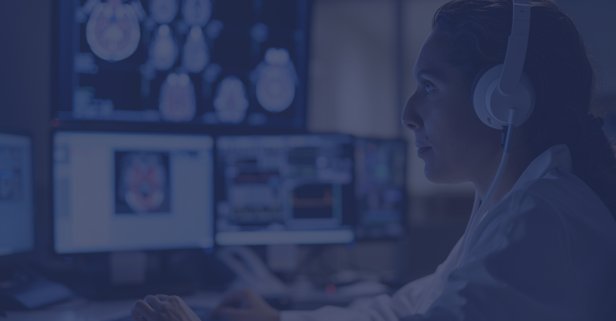 Healthcare clinician sat in front of multiple screens with patient scans and headphones